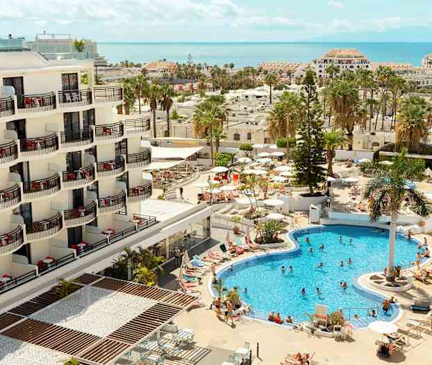 Ett hotell med balkonger och en poolområde med besökare och parasoller. (AI-genererad text)