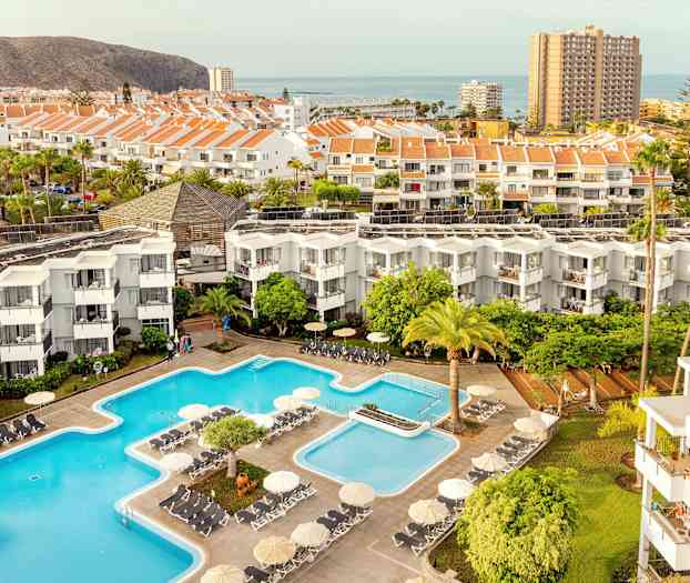 Vy över hotellområde med pooler, byggnader och omgivande landskap. (AI-genererad text)