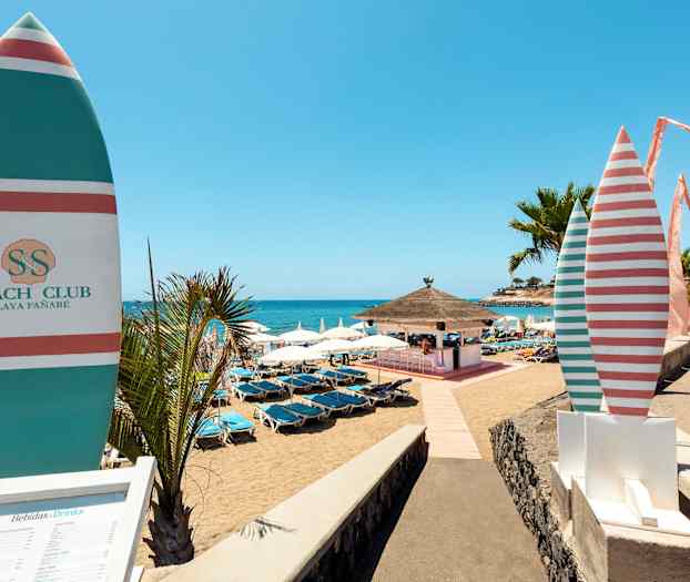 En solig strand med parasoller och solstolar, en strandbar syns i bakgrunden. (AI-genererad text)