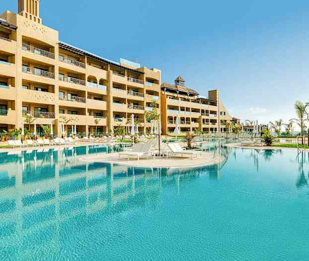 Hotellets utomhuspool med solstolar och omgivande byggnader. (AI-genererad text)