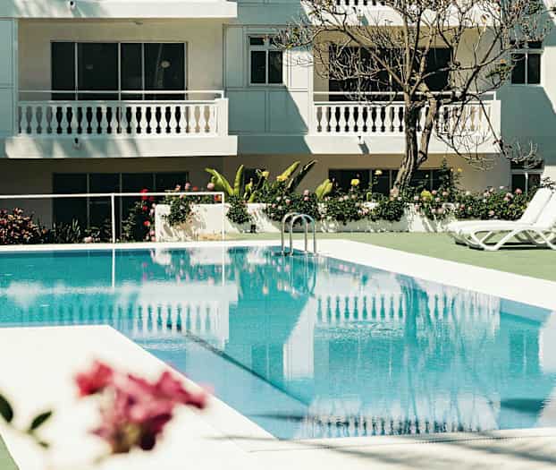 Utomhuspool med solstolar vid ett vitmålat hotell. (AI-genererad text)