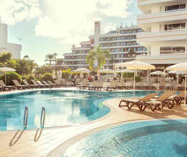 Hotellpool med solstolar och parasoller, omgivet av byggnader. (AI-genererad text)