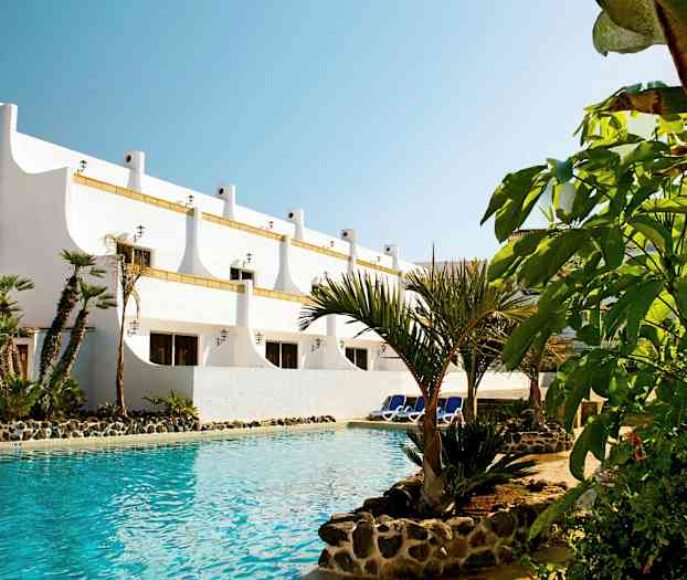 Vit byggnad med palmträd vid en pool. (AI-genererad text)