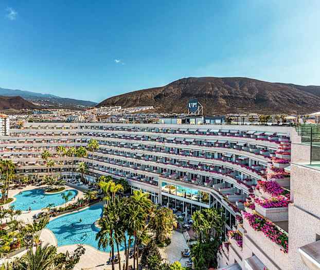 Bild av hotellkomplex med poolområde och omgivande berg. (AI-genererad text)