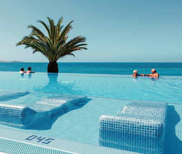 En infinitypool med utsikt över havet, med en palm i mitten och badgäster som simmar. (AI-genererad text)