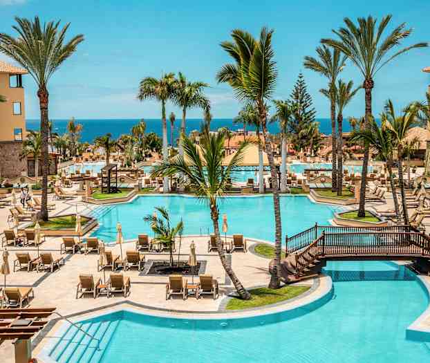 Hotellpoolområde med solstolar, palmer och havsutsikt. (AI-genererad text)