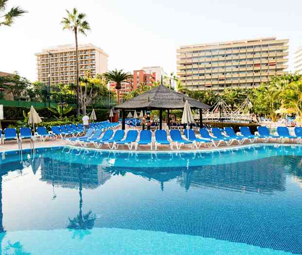 En pool med solstolar runtom och hotellbyggnader i bakgrunden. (AI-genererad text)