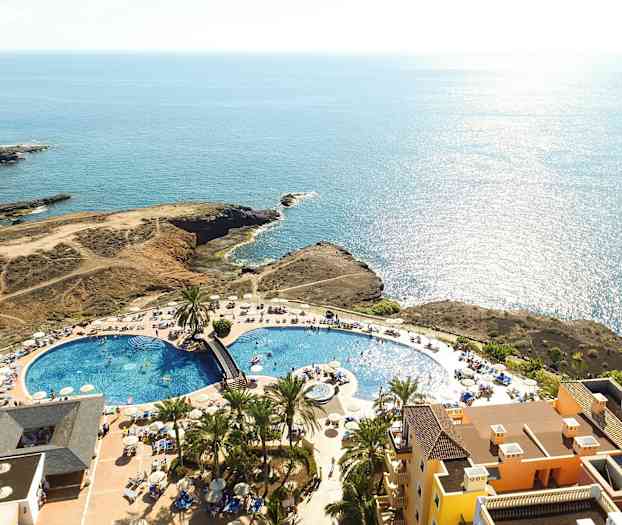 Flygbild av en resort med pool, solstolar och havsutsikt. (AI-genererad text)