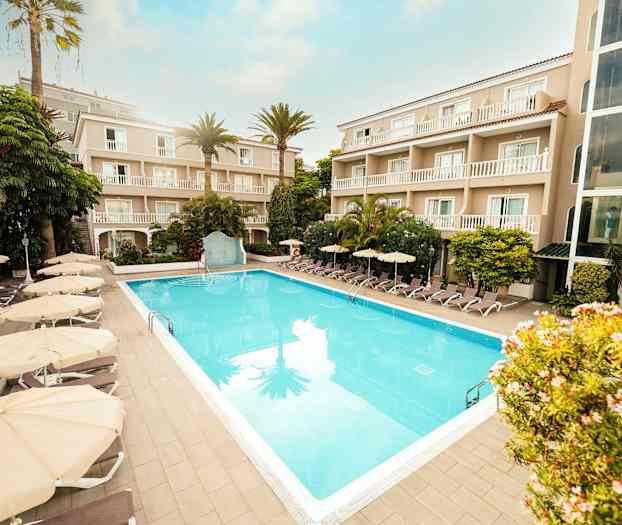 Hotellområde med en utomhuspool omgiven av solstolar och parasoller samt byggnader med balkonger. (AI-genererad text)