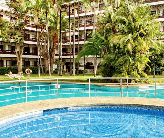 Utomhuspool framför en hotellbyggnad med balkonger och grönskande träd. (AI-genererad text)