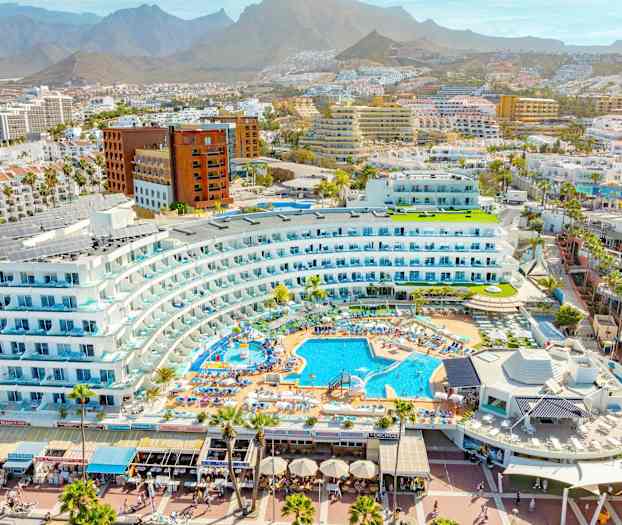 Vy över ett semesterkomplex med pooler och omgivande bebyggelse i en bergig miljö. (AI-genererad text)