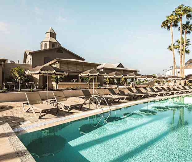 Bild av ett poolområde med solstolar, parasoller och en byggnad i bakgrunden. (AI-genererad text)