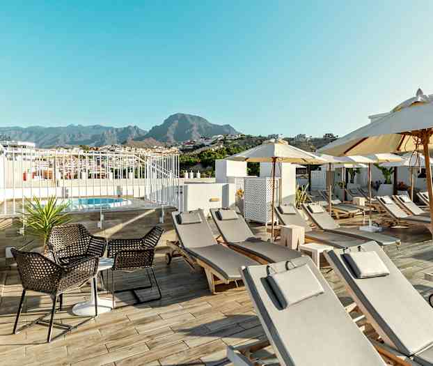 Pool med solstolar och parasoller på en hotellterrass med berg i bakgrunden. (AI-genererad text)