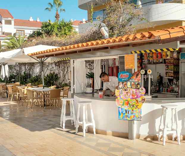 En uteservering med bord och parasoll bredvid en bar. (AI-genererad text)