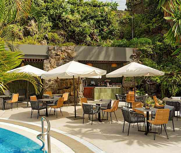 Uteservering vid poolen med bord, stolar och parasoller. Bakgrunden har grön växtlighet och en mindre bar. (AI-genererad text)