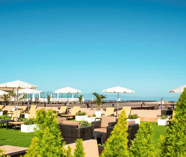 Takterrass med solsängar, parasoller och växter mot en klarblå himmel. (AI-genererad text)