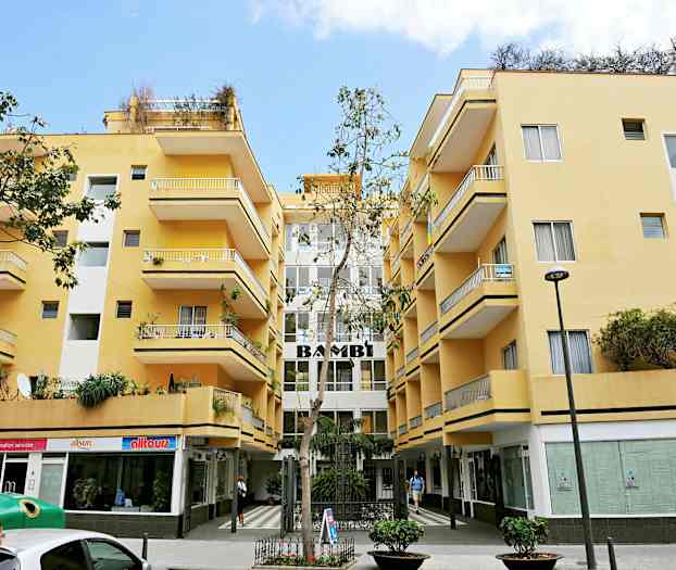 Gul byggnad med balkonger och butiker på bottenvåningen. (AI-genererad text)