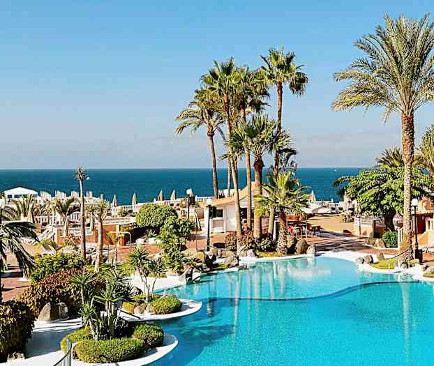 En semesterort med en pool, omgiven av palmträd och med utsikt över havet i bakgrunden. (AI-genererad text)