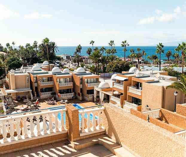 Utsikt över hotellbyggnader och en pool med havet i bakgrunden. (AI-genererad text)