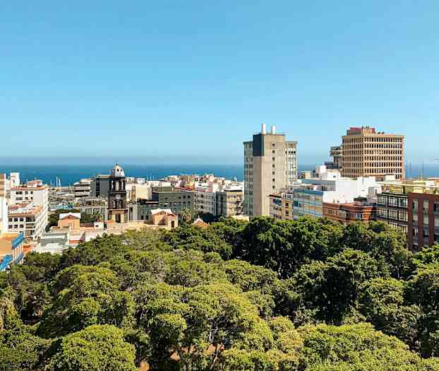 Stadsvy med byggnader och grönområde, havet syns i bakgrunden. (AI-genererad text)
