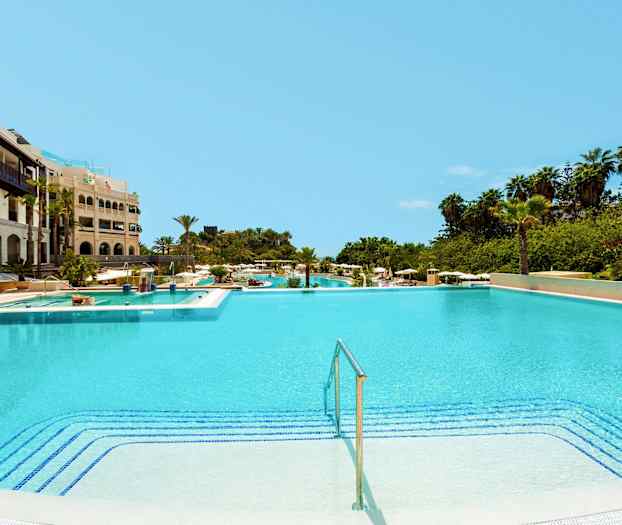 Stor swimmingpool vid ett hotell med omgivande grönska. (AI-genererad text)