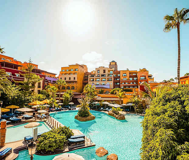 Semesteranläggning med pool, solstolar och färgglada hotellanläggningar under klarblå himmel. (AI-genererad text)