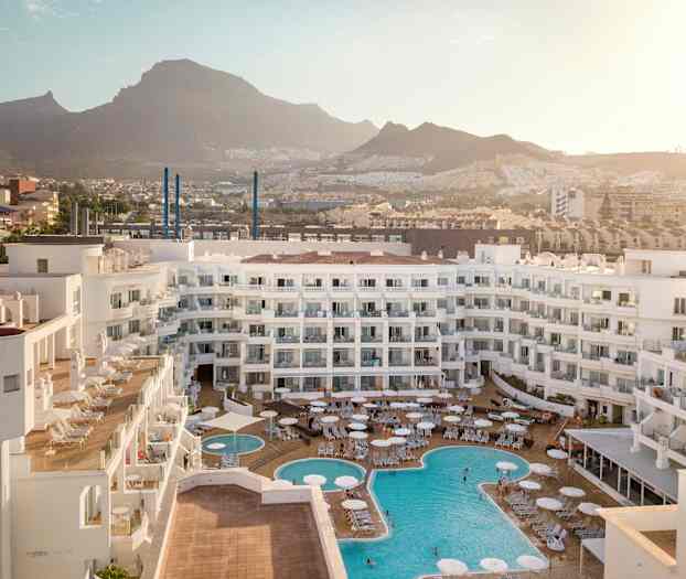 Vy över hotellområde med pooler och omgivande berg. (AI-genererad text)