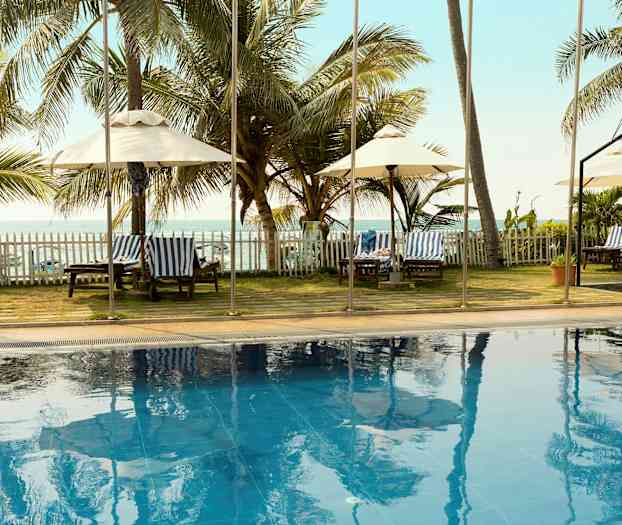 En utomhuspool med palmer och solstolar i bakgrunden, samt havsutsikt. (AI-genererad text)