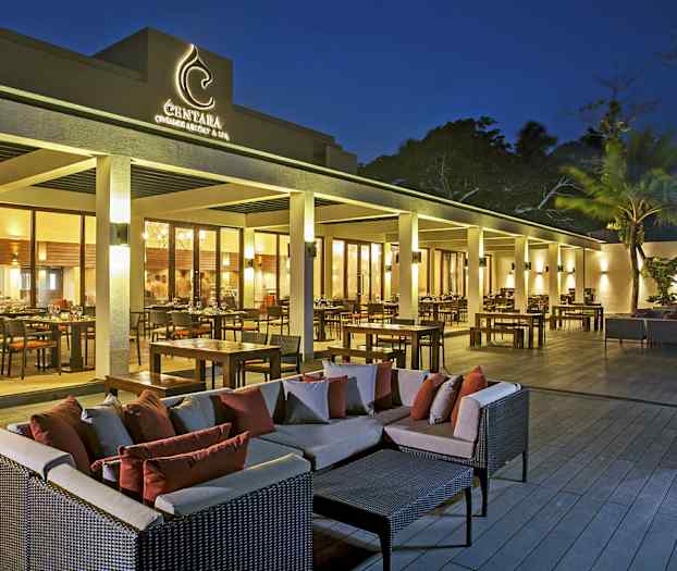 En utomhusterrass vid en restaurang med bord, stolar och soffgrupper i skymningsljus. (AI-genererad text)