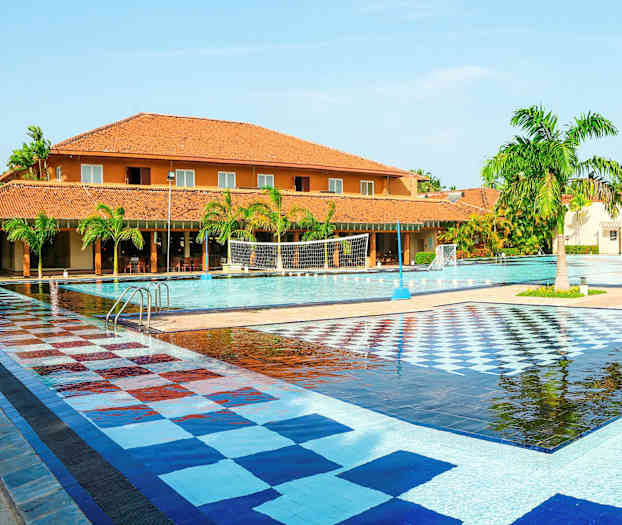 En stor utomhuspool med kaklad färgglad yta, omgiven av palmer och byggnader med tegelfärgade tak. (AI-genererad text)