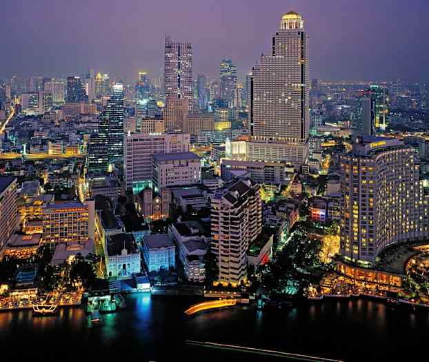 En stadsvy på kvällen upplyst av byggnader och gatubelysning, med en flod i förgrunden. (AI-genererad text)