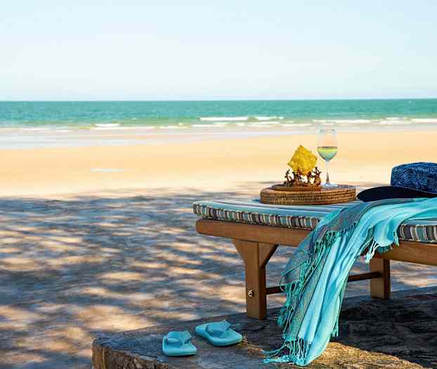 Solstol med en hatt, handduk och flip-flop-sandaler vid stranden. (AI-genererad text)