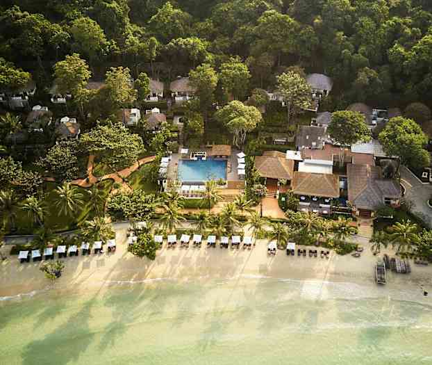 Flygfoto över en badort vid stranden med palmer, solstolar och en pool, omgiven av frodig grönska. (AI-genererad text)