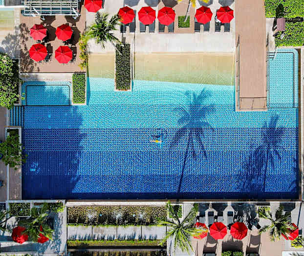 Flygfoto av en utomhuspool omgiven av solstolar och parasoller. (AI-genererad text)