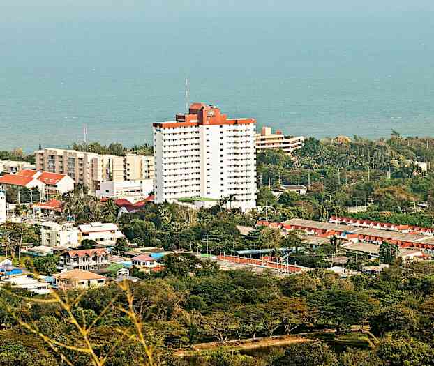 En stad vid kusten med flera byggnader, inklusive en hög vit byggnad med röd takdel och hav i bakgrunden. (AI-genererad text)