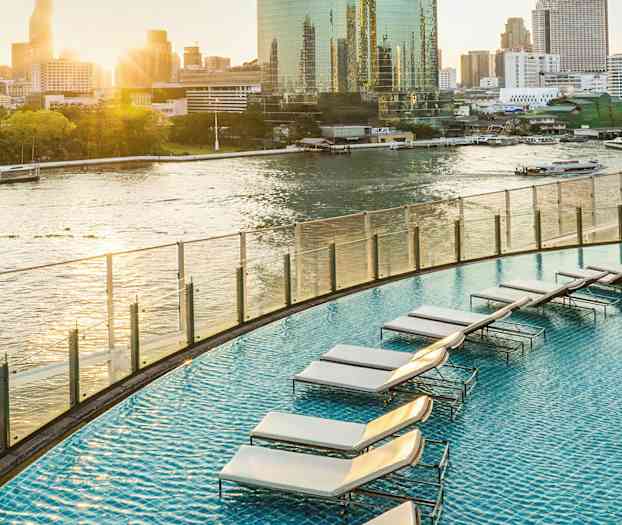 En swimmingpool på en högterrass med utsikt över en flod i en stadsmiljö. (AI-genererad text)