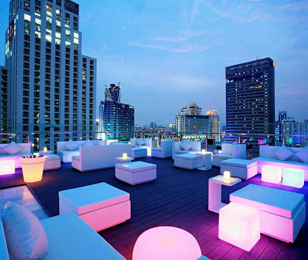 En takterrass med moderna möbler och färgglad belysning, omgiven av höghus på kvällen. (AI-genererad text)