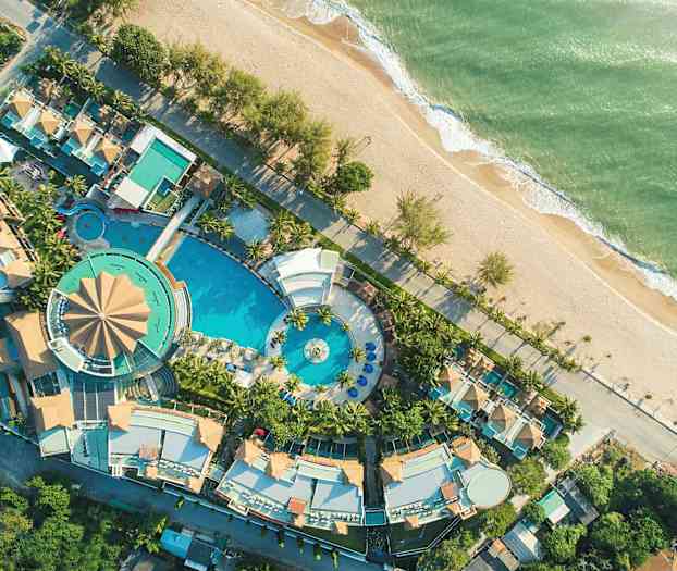 Flygfoto av en resort med poolområde och omgivande byggnader vid stranden. (AI-genererad text)