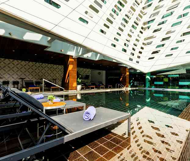 Ett modernt utomhusområde med en pool, solstolar och ett tak täckt av geometriska öppningar. (AI-genererad text)