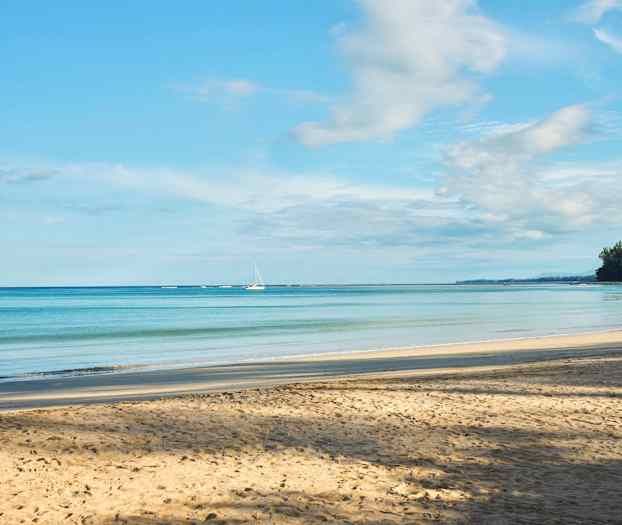 En sandstrand med en lugn havsutsikt, två segelbåtar vid horisonten och trädförsedda kuster till höger. (AI-genererad text)
