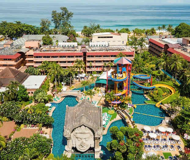 Friluftsområde med vattenpark, pool och grönytor framför byggnader vid havet. (AI-genererad text)