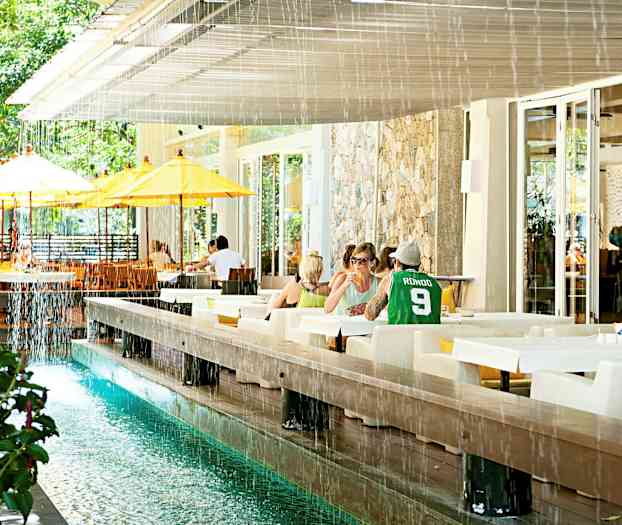 Ett utomhusområde med bord och stolar, samt en vattenkanal och gulvita parasoller. (AI-genererad text)