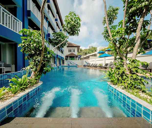 En pool med grönskande växter omgiven av byggnad och solstolar. (AI-genererad text)