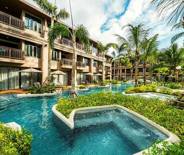 Exteriör av ett hotell med flera våningar, omgärdat av palmer och med poolområden som slingrar sig genom miljön. (AI-genererad text)