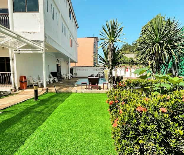 En utomhusbild av en byggnad med en grön gräsmatta och omgivande växter. (AI-genererad text)