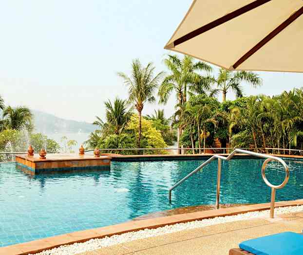 En utomhuspool med utsikt över gröna palmer och skogsklädda kullar, med solstolar och ett parasoll i förgrunden. (AI-genererad text)