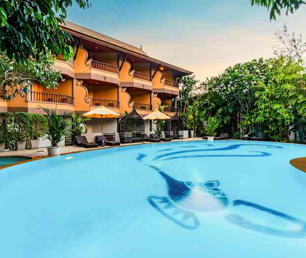 En pool med klart vatten, omgiven av solstolar, parasoller och grönska. Ett hotell med balkonger syns i bakgrunden. (AI-genererad text)