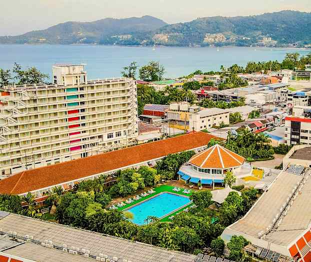 Vy över ett hotellområde med en vit flervåningsbyggnad, en swimmingpool, och en utsikt mot havet. (AI-genererad text)