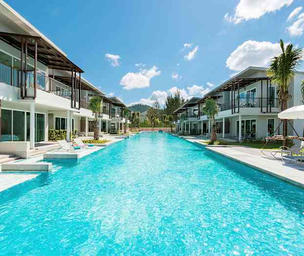 Utsikt över en lång pool omgiven av moderna villor och solstolar under parasoller. (AI-genererad text)