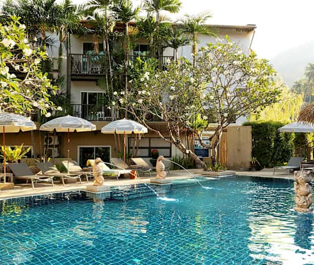 Poolområde med parasoller och solstolar framför ett hotell. (AI-genererad text)